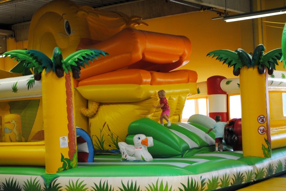 Aufblasbare Hüpfburg mit Riesenente und Palmen, Kinder spielen darauf.