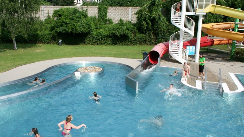 Ein Freibad mit Wasserrutsche und mehreren Personen im Wasser.