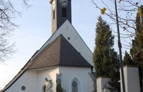 Gotische Kirche in Kirchstetten mit Turm und Statue im Vordergrund.