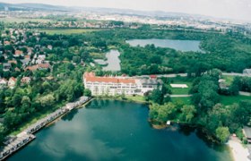 Luftaufnahme von Brunn am Gebirge mit einem großen Gebäude am See und grüner Landschaft.