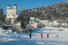 Winterlandschaft mit Kirche und Skilangläufern.