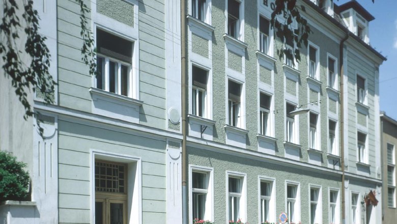 Au&szlig;enansicht eines mehrst&ouml;ckigen Geb&auml;udes mit gr&uuml;ner Fassade und wei&szlig;en Fensterrahmen.