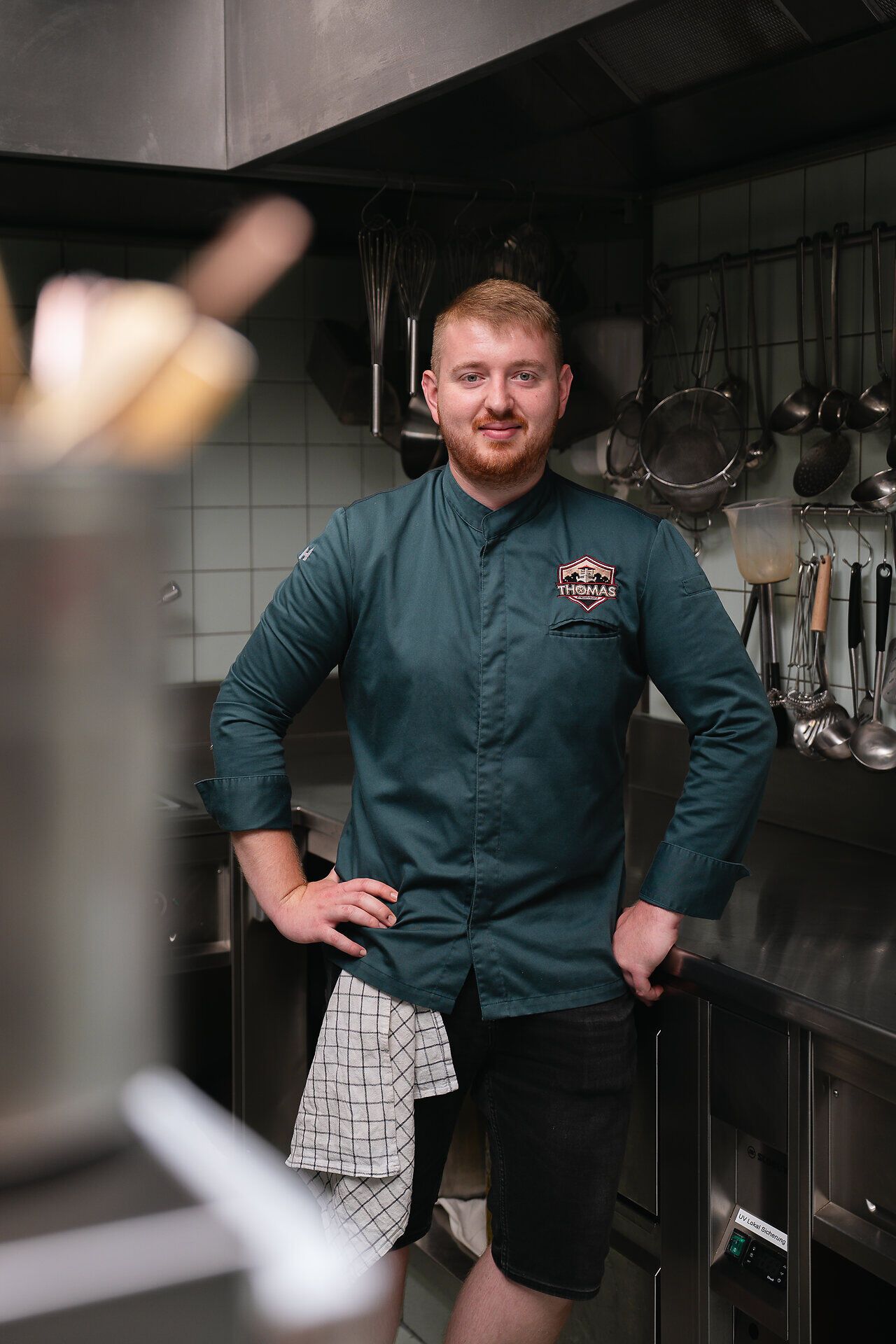 Thomas Reinisch steht in der Küche im Lokal Thomas im Johanneshof, blickt in die Kamera, Arme an die Hüfte gelehnt.