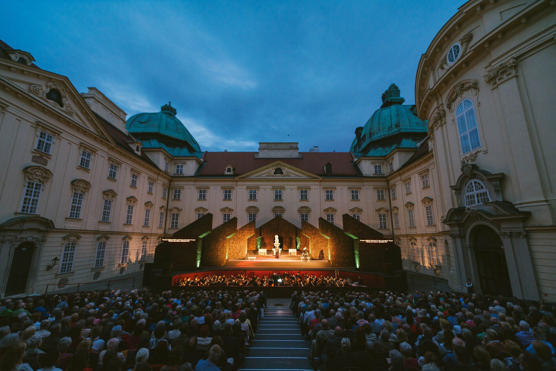 In der malerischen Kulisse eines historischen Klosters versammeln sich Menschen, um die Magie des Theaters unter freiem Himmel zu erleben. Die sanften Klänge der Darbietungen vermischen sich mit dem Duft von frischem Gras und den sanften Farben des Abendhimmels, während die Zuschauer gebannt den Geschichten lauschen. Ein unvergesslicher Abend, der die Seele berührt und die Schönheit der Kultur feiert.
