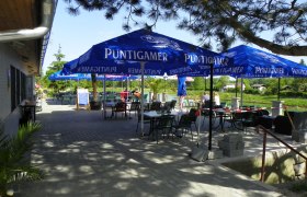 Außenbereich eines Gasthauses mit blauen Sonnenschirmen und Tischen.