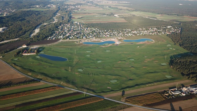 Aerial view of a golf course with several water hazards and adjacent settlement.