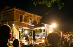 Ein lebendiges Treiben erfüllt die Nacht, während die Lichter des Kulturbahnhofs in Altenmarkt strahlen. Die Menschen versammeln sich, um die kulturellen Darbietungen zu genießen und die besondere Atmosphäre des Kultursommers Wienerwald zu erleben.