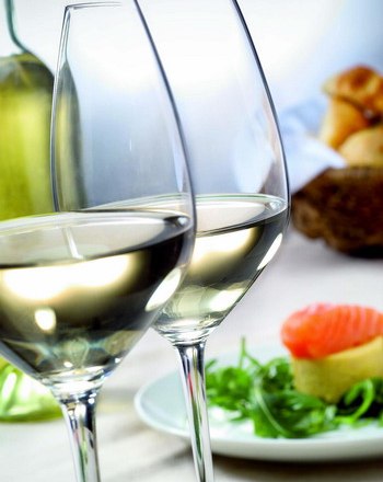 Zwei gefüllte Weingläser mit Weißwein, im Hintergrund ein Teller mit Lachs und Salat.