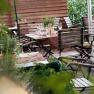 A cozy guest garden with wooden tables and chairs, set with glasses and cutlery, surrounded by plants.