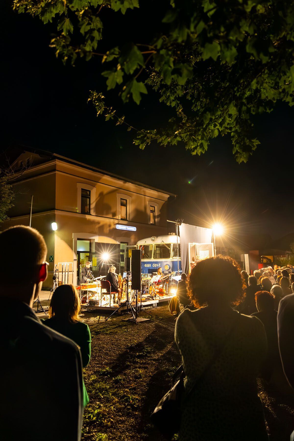 Ein lebendiges Treiben erfüllt die Nacht, während die Lichter des Kulturbahnhofs in Altenmarkt strahlen. Die Menschen versammeln sich, um die kulturellen Darbietungen zu genießen und die besondere Atmosphäre des Kultursommers Wienerwald zu erleben.
