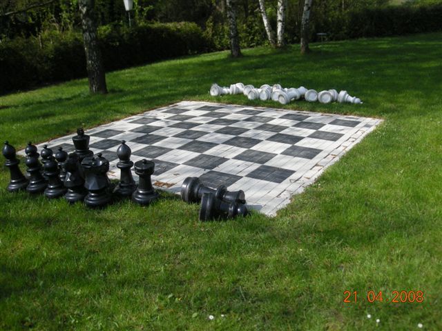 Großes Schachbrett im Freien mit schwarzen und weißen Figuren auf einer Wiese.