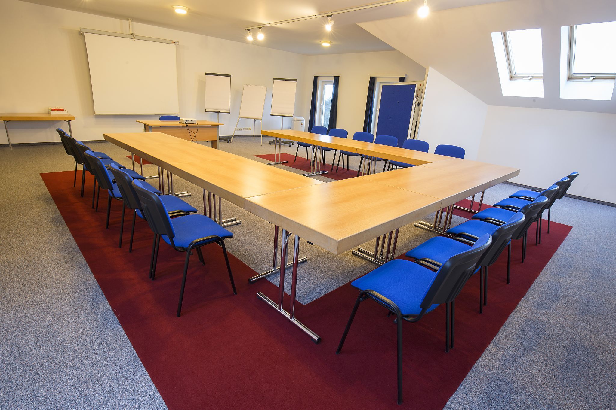 Konferenzraum mit U-förmigem Tisch und blauen Stühlen.