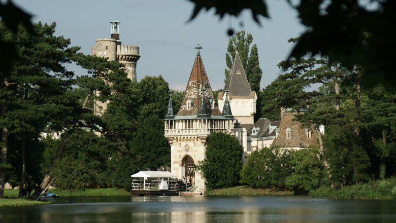 Schloss Laxenburg mit Türmen und Bäumen am Seeufer.