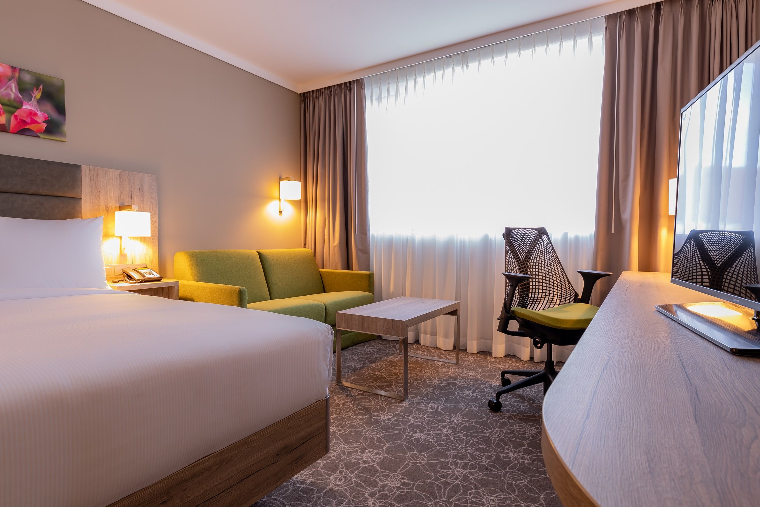 Hotelzimmer mit Bett, grünem Sofa, Schreibtisch und Stuhl.