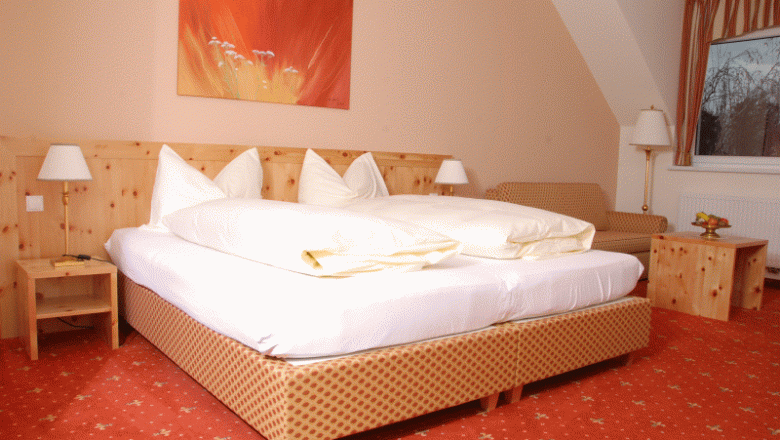 Gemütliches Hotelzimmer mit Doppelbett, Holzmöbeln und rotem Teppich.