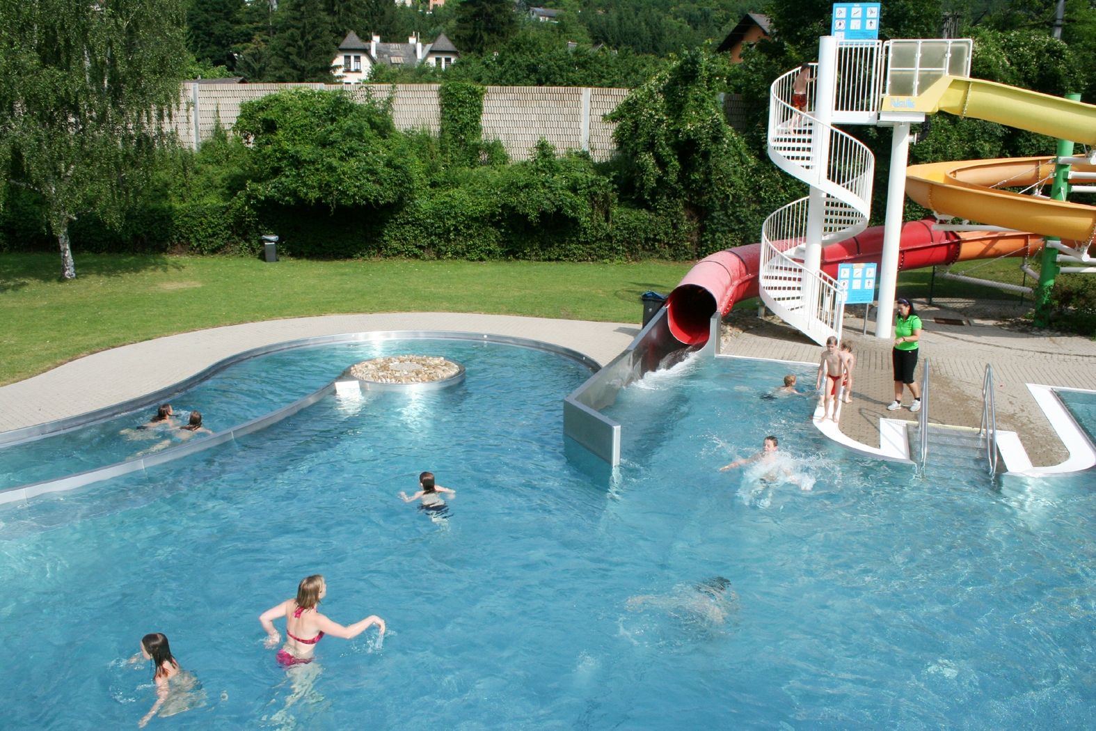 Ein Freibad mit Wasserrutsche und mehreren Personen im Wasser.