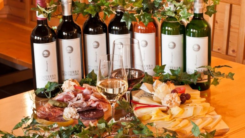 Weinflaschen und kalte Platten mit Käse und Wurst auf einem Tisch.