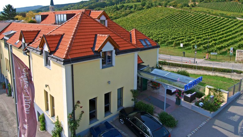 Außenansicht des Hotel Turmhof mit roten Dächern und umliegenden Weinbergen.
