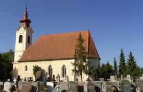 Außenansicht einer Kirche mit Friedhof im Vordergrund und blauem Himmel.