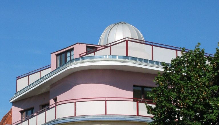 A modern building with a dome on the roof, surrounded by trees, under a clear blue sky.