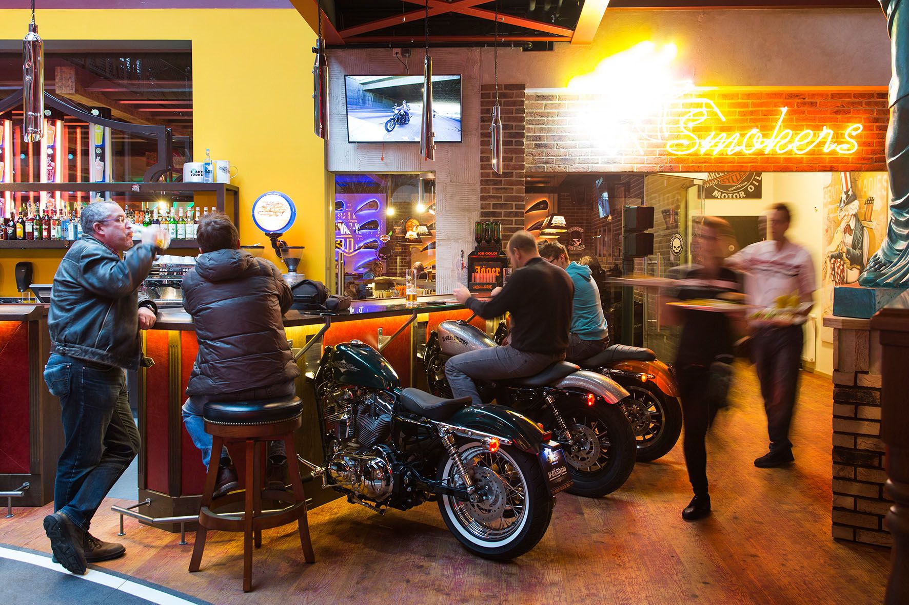 Bar mit Motorrädern als Sitzgelegenheiten, Neonlicht und Gästen.