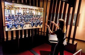 Person dirigiert virtuelles Orchester auf Bildschirm im Haus der Musik.