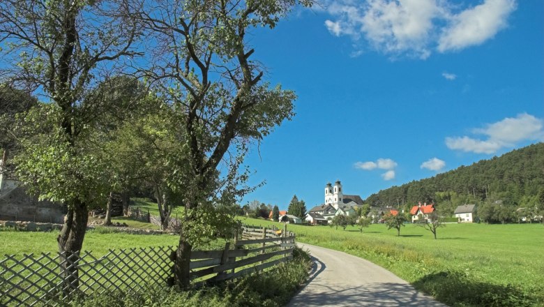 Landschaft mit Kirche und Bäumen unter blauem Himmel.