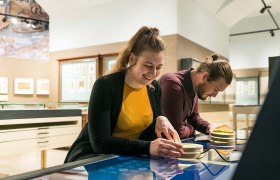 Zwei Personen interagieren mit einem interaktiven Display im Papyrusmuseum.