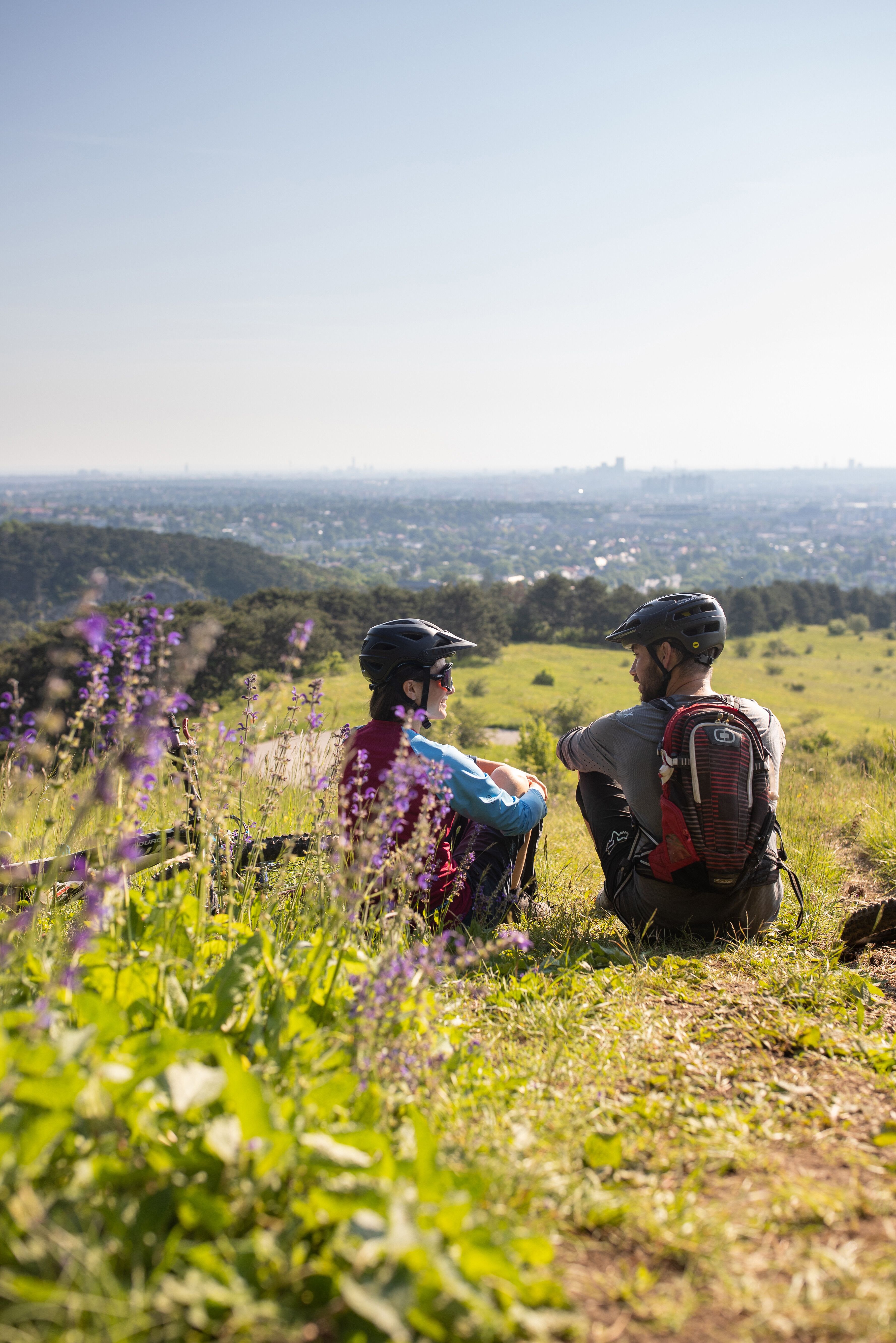 Zwei Mountainbiker genießen die atemberaubende Aussicht über die sanften Hügel und das weite Tal. Umgeben von bunten Wildblumen und der frischen Sommerluft, erleben sie einen perfekten Moment der Ruhe und Verbundenheit mit der Natur.