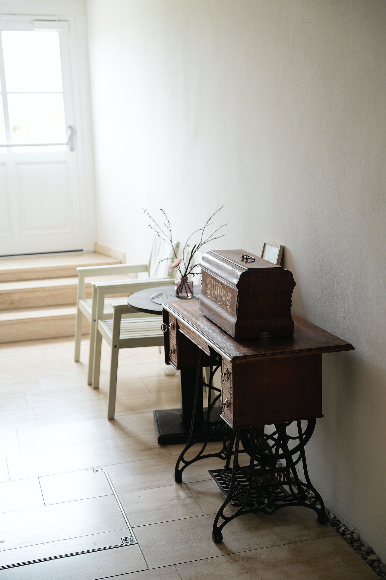 Im Eingangsbereich des Weinkellers im Freigut Thallern steht ein rustikaler Holztisch und darauf eine alten Holztruhe. Der Bereich ist hell gestaltet und lädt Besucher mit seinem charmanten, historischen Flair ein.