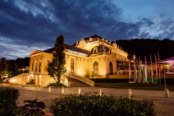 Beleuchtetes Casino Baden bei Nacht mit dramatischem Himmel.