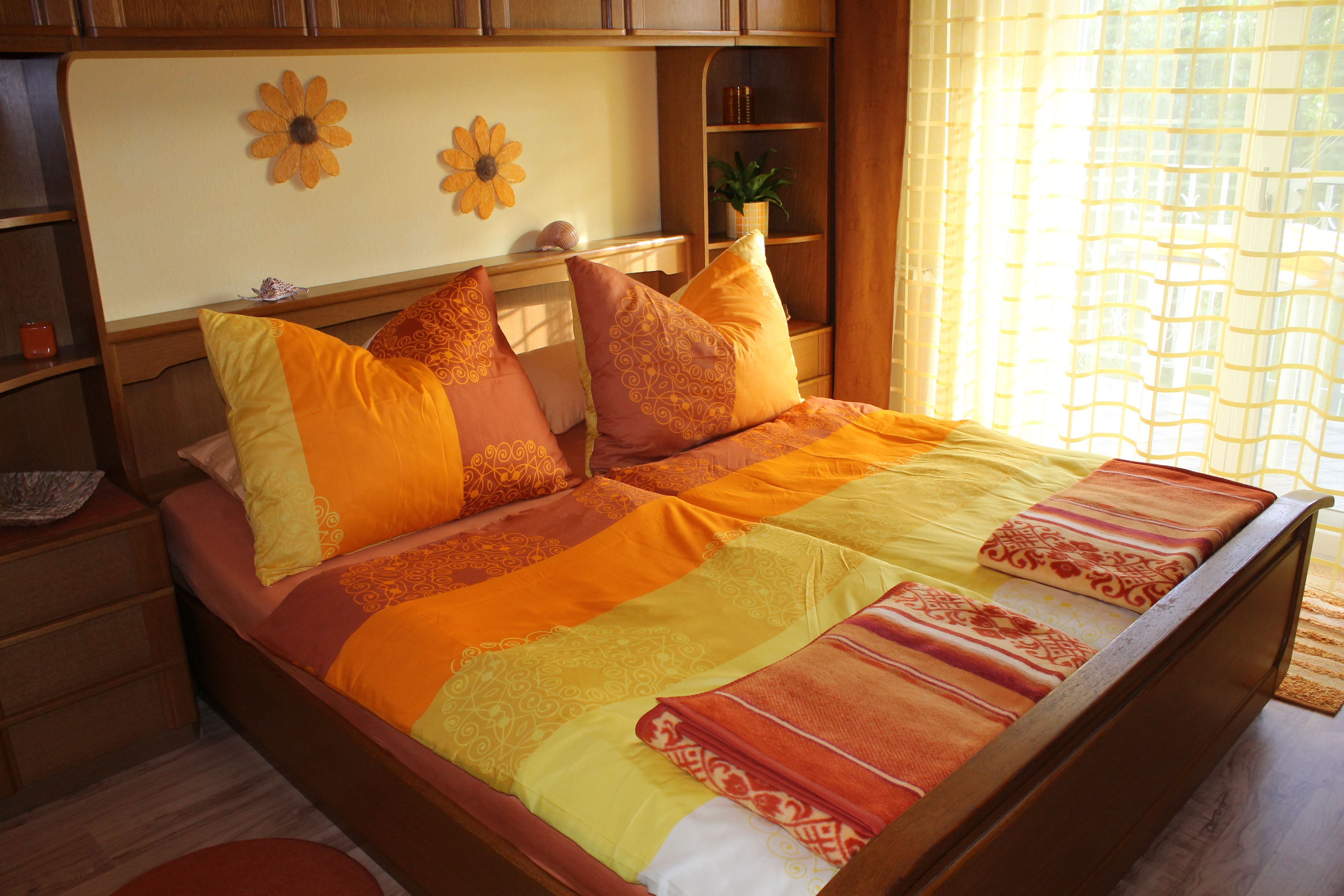 Gemütliches Schlafzimmer mit Sonnenblumen-Dekor und orange-gelber Bettwäsche.