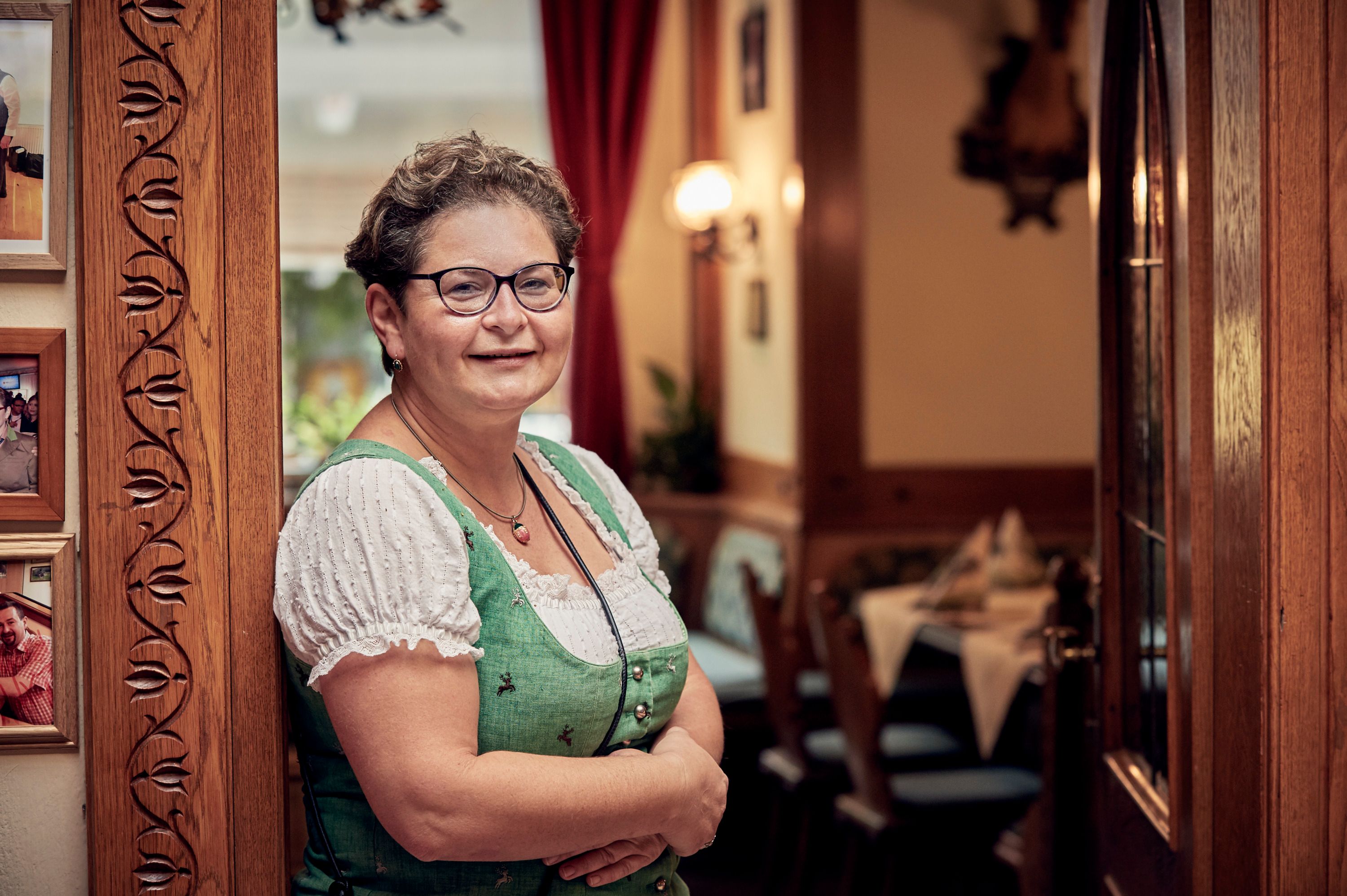 Eine Frau in traditioneller Kleidung steht lächelnd in einem gemütlichen Gastraum.