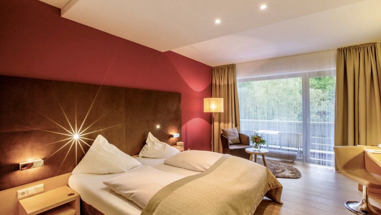 Modernes Hotelzimmer mit Doppelbett, roter Wand, großem Fenster und Sitzbereich.