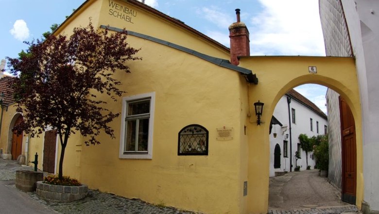 Gelbes Gebäude mit der Aufschrift 'Weinbau Schabl', daneben ein Torbogen und ein Baum.