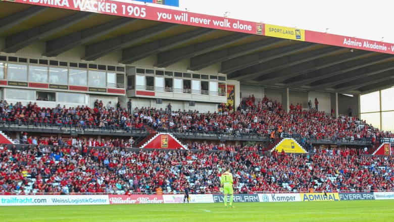 Fußballstadion mit vollen Tribünen und einem Spieler auf dem Spielfeld.
