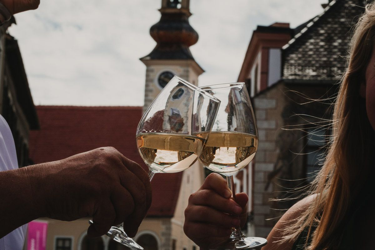 Genussvolle Momente im Herzen von Mödling: Eine festlich gekleidete Frau und ein Mann stoßen mit Weißwein an.