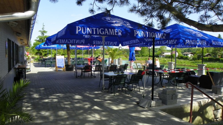 Außenbereich eines Gasthauses mit blauen Sonnenschirmen und Tischen.