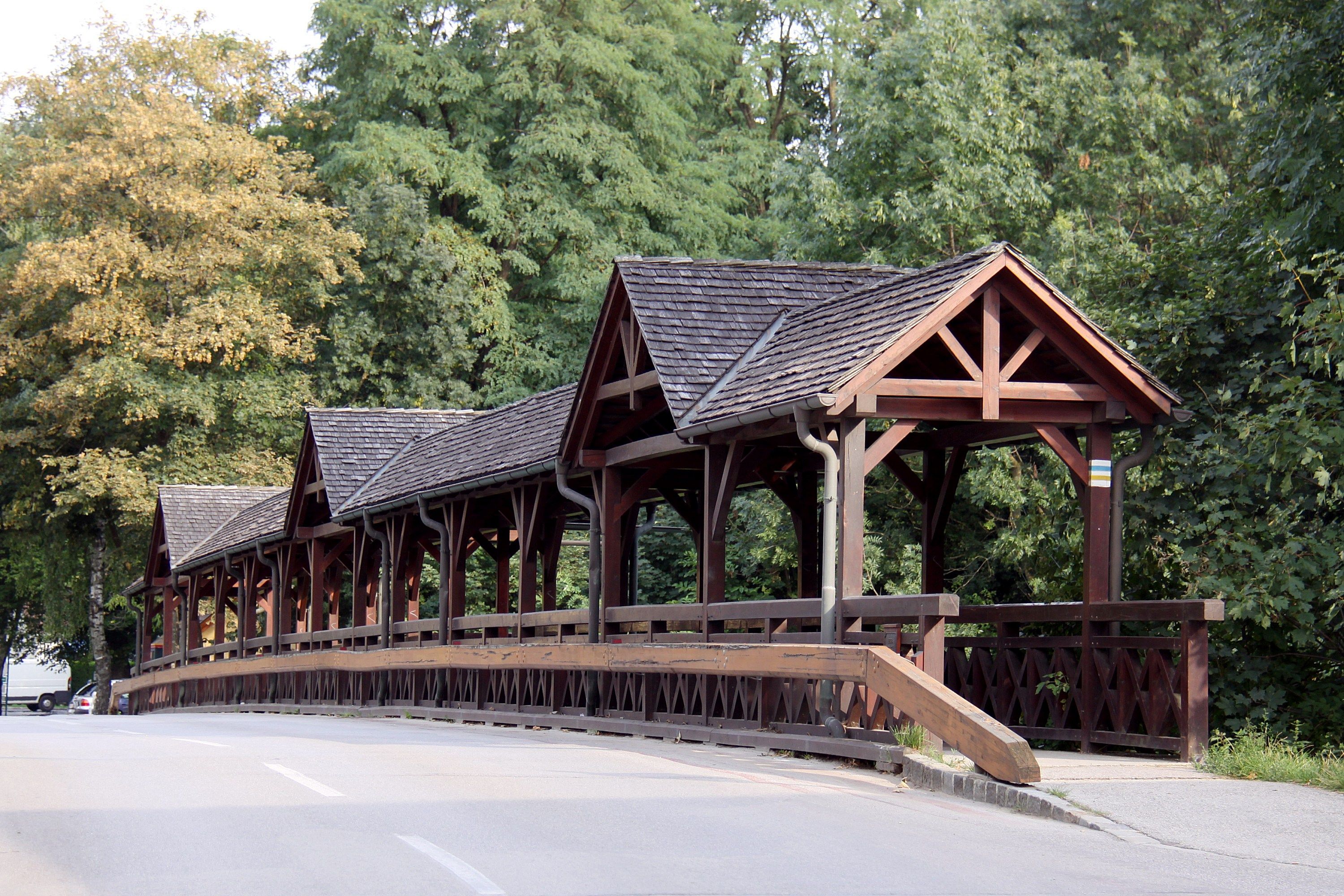 Holzbrücke mit überdachtem Gehweg in einer grünen Umgebung.