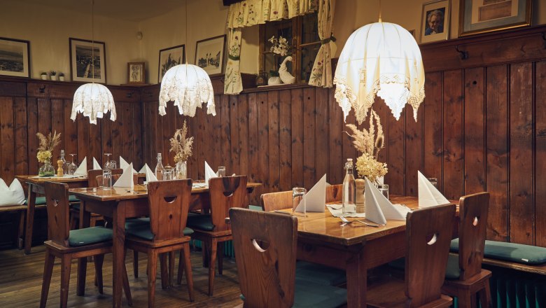 Gemütliche Stube mit Holzmöbeln, Tischdekoration und hängenden Lampen.