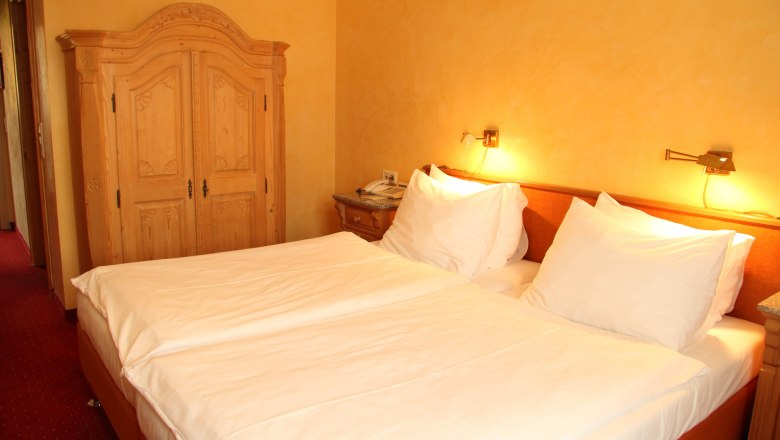 Hotel room with double bed, wooden furniture and warm light.
