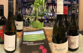 Wine bottles and glasses on a table with a brochure of the Thermenregion wine region.