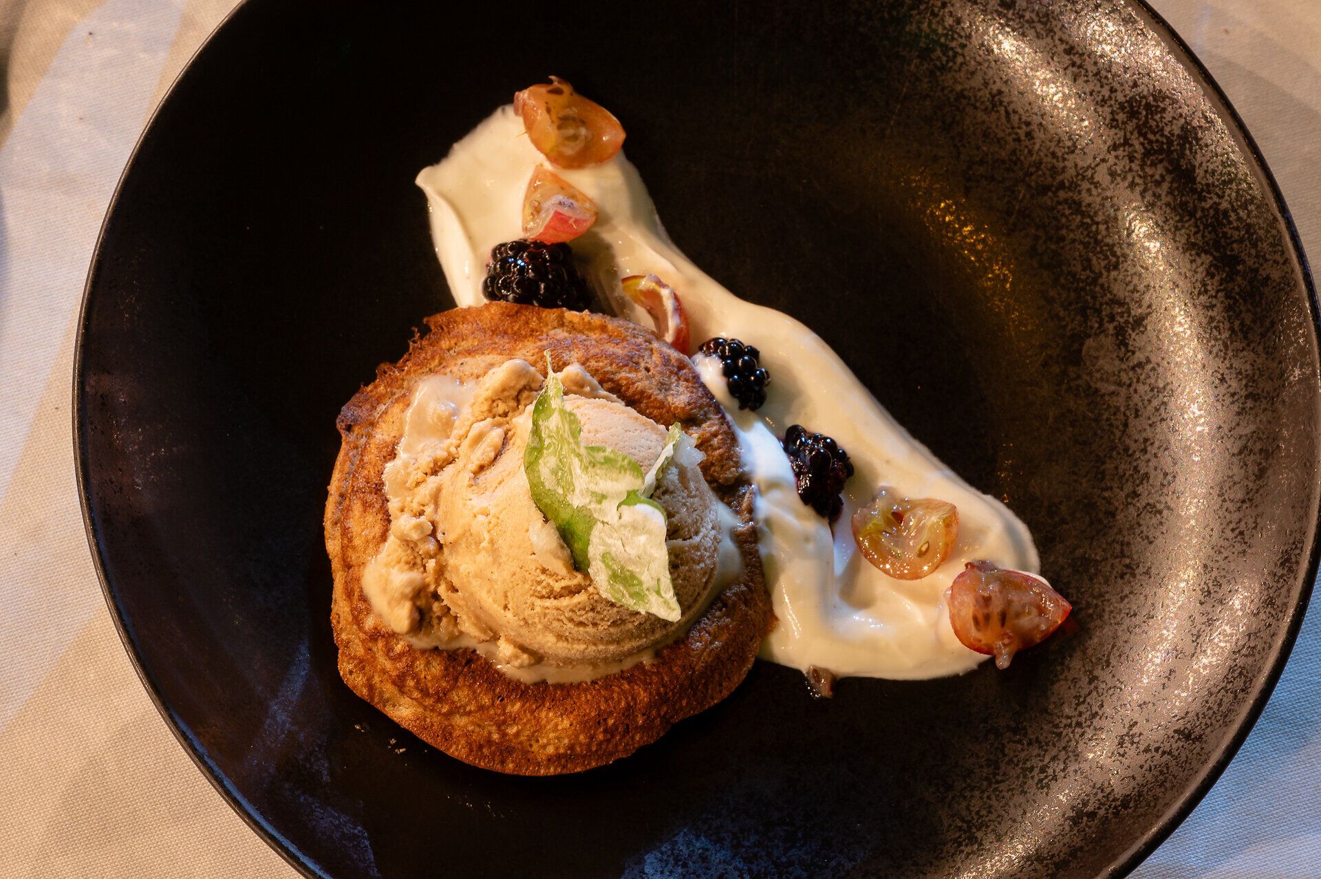 Hausgemachte Eicheldalken mit Eichelkaffee-Eis Stachelbeeren & Brombeeren, kandierten Eichenblättern auf einem schwarzen Porzellanteller angerichtet.