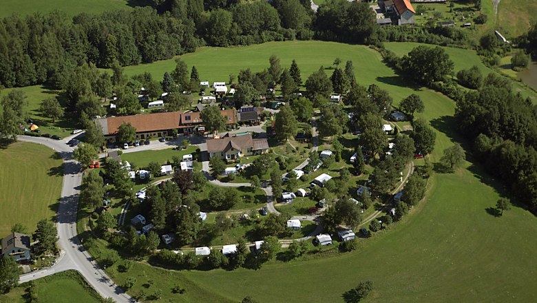 Aerial view of a campsite in the middle of a green landscape with caravans and tents.
