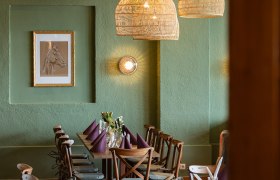 Gemütlicher Essbereich mit Holztisch, Stühlen und geflochtenen Lampen.