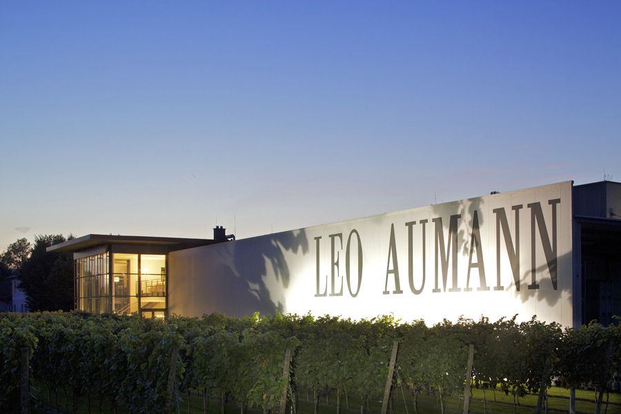 Gebäude mit der Aufschrift 'Leo Aumann' bei Dämmerung, umgeben von Weinreben.