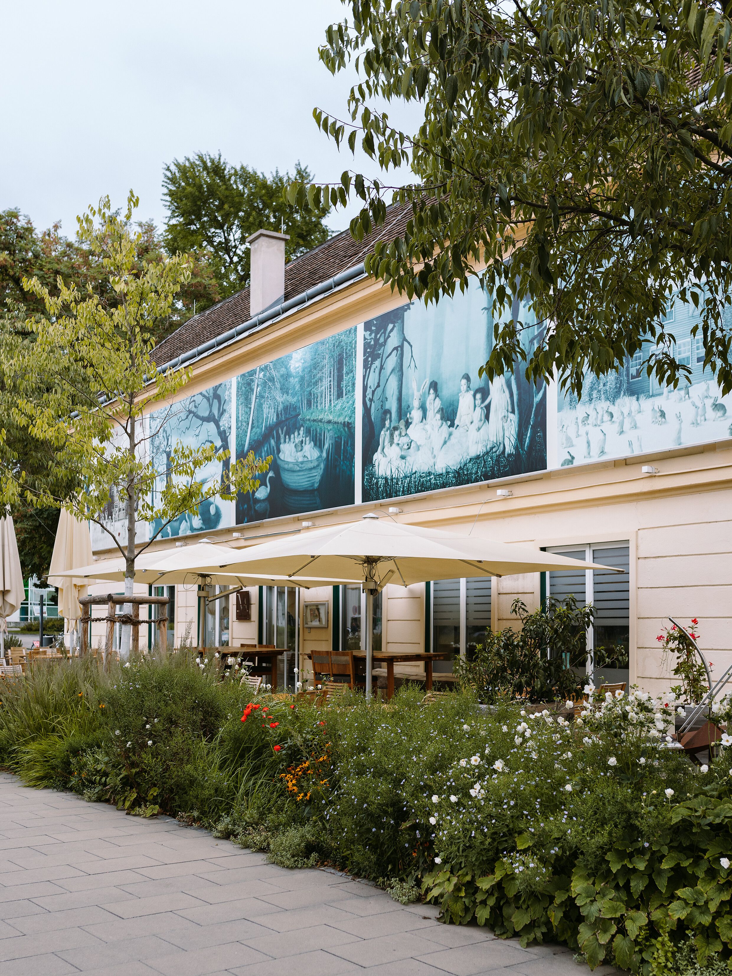 Inmitten der blühenden Gärten und unter schattenspendenden Bäumen entfaltet sich eine Oase der Ruhe. Die sanften Farben der Blumen und das beruhigende Rauschen der Blätter laden dazu ein, die Seele baumeln zu lassen und die Schönheit des Sommers zu genießen.