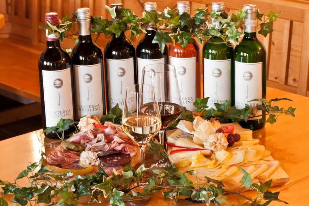 Weinflaschen und kalte Platten mit Käse und Wurst auf einem Tisch.