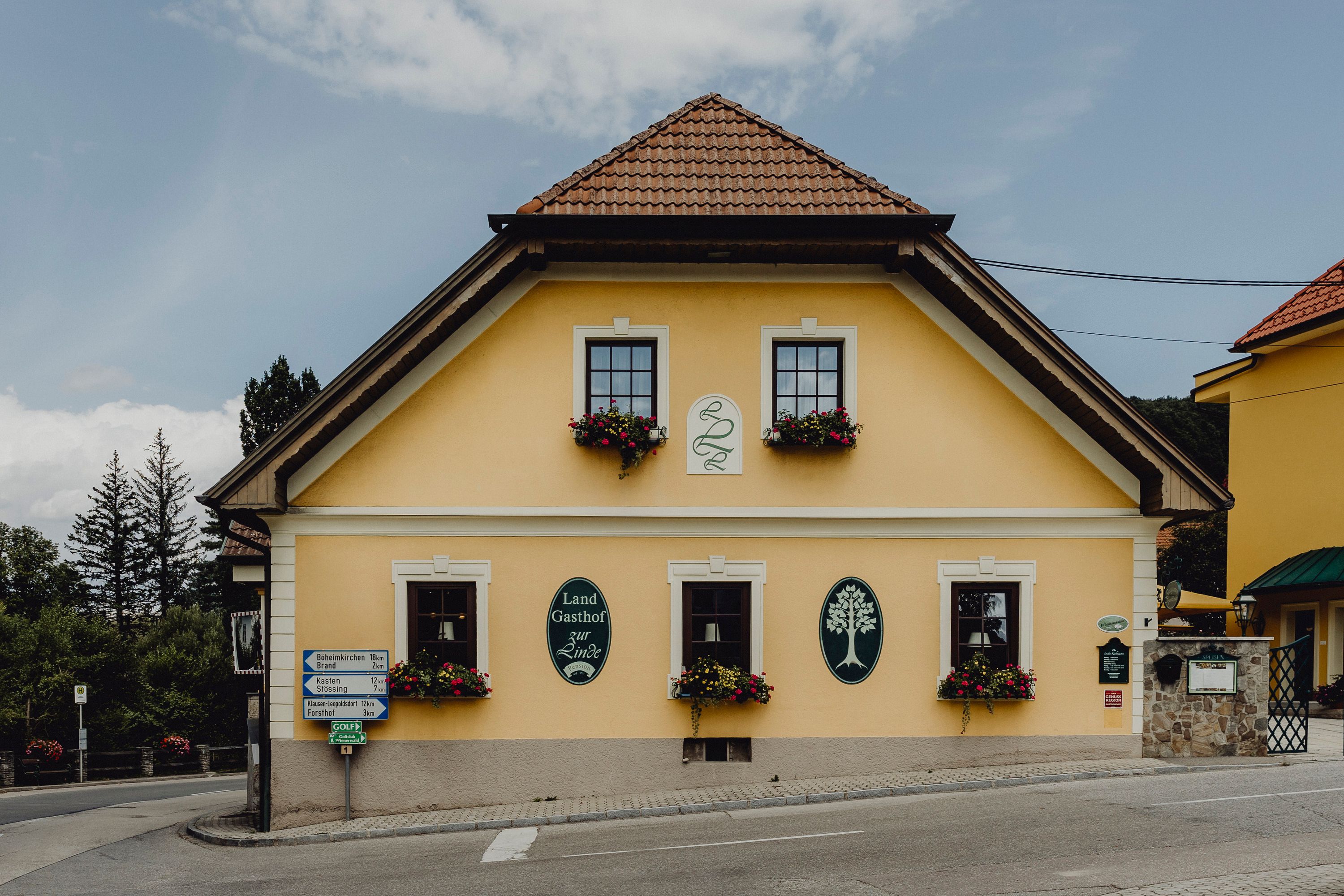 Gelbes Gasthaus mit Blumenkästen und Schildern an der Fassade.