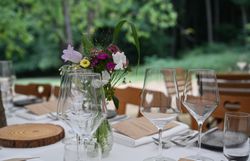 Schön gedeckter Tisch am Waldrand, darauf zu sehen ist ein weißes Tischtuch und frischer Blumenschmuck.